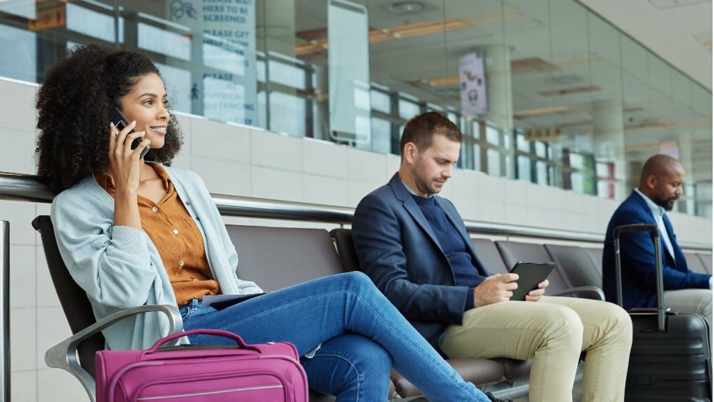 Travelers at an airport using their phones and tablets while they wait for their plane.