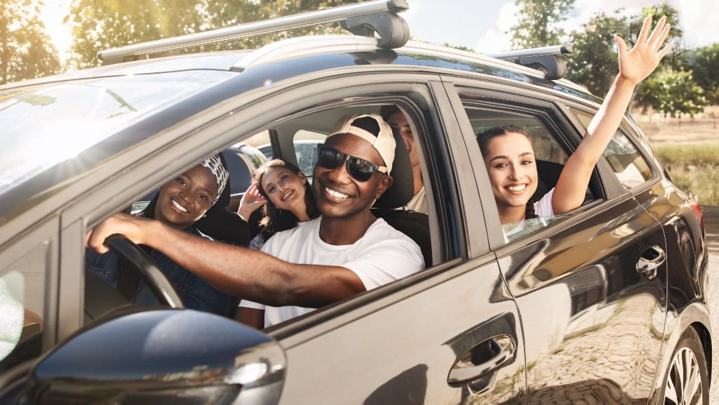 Man driving his friends around. The windows are rolled down and everyone is smiling.