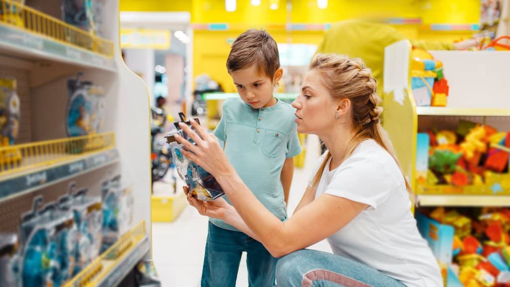 Mom with her young son in a toy store looking at the price of toys together.