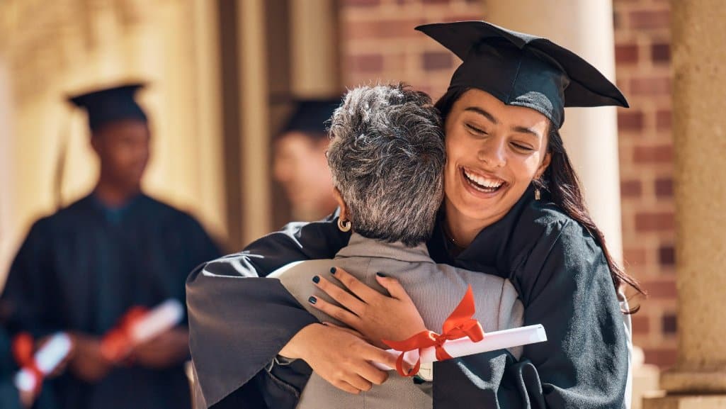 College graduate in cap and gown hugging her professor.