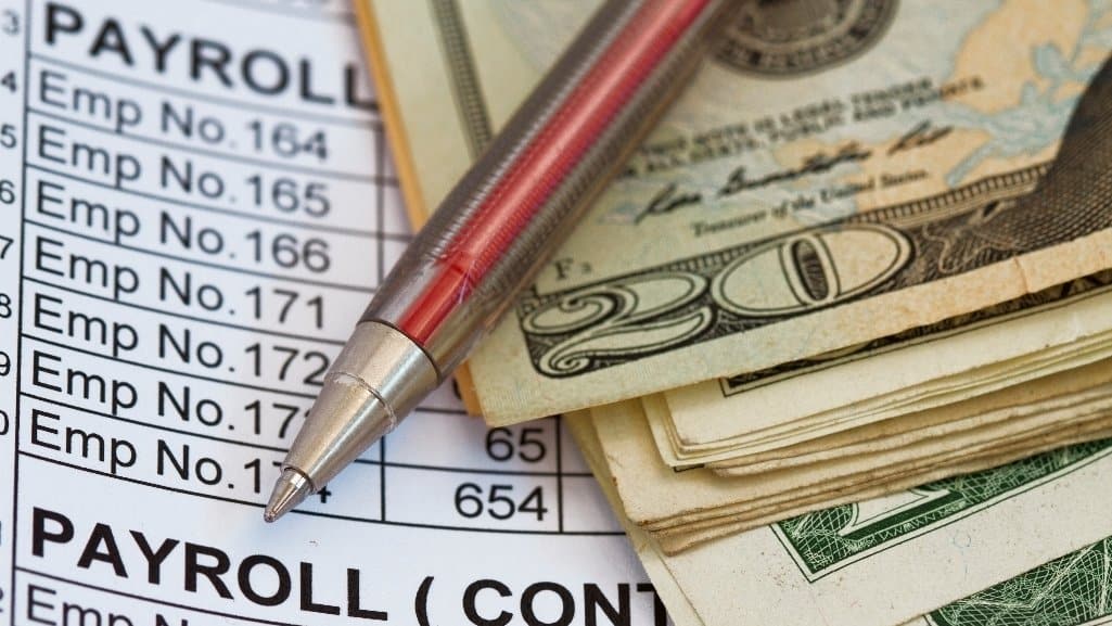 A pen and cash on top of a payroll sheet.