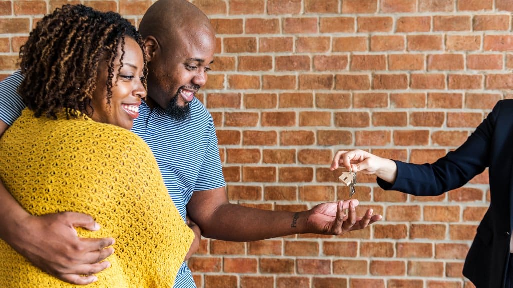 Happy couple is all smiles as their realtor hands them the keys to their new house.