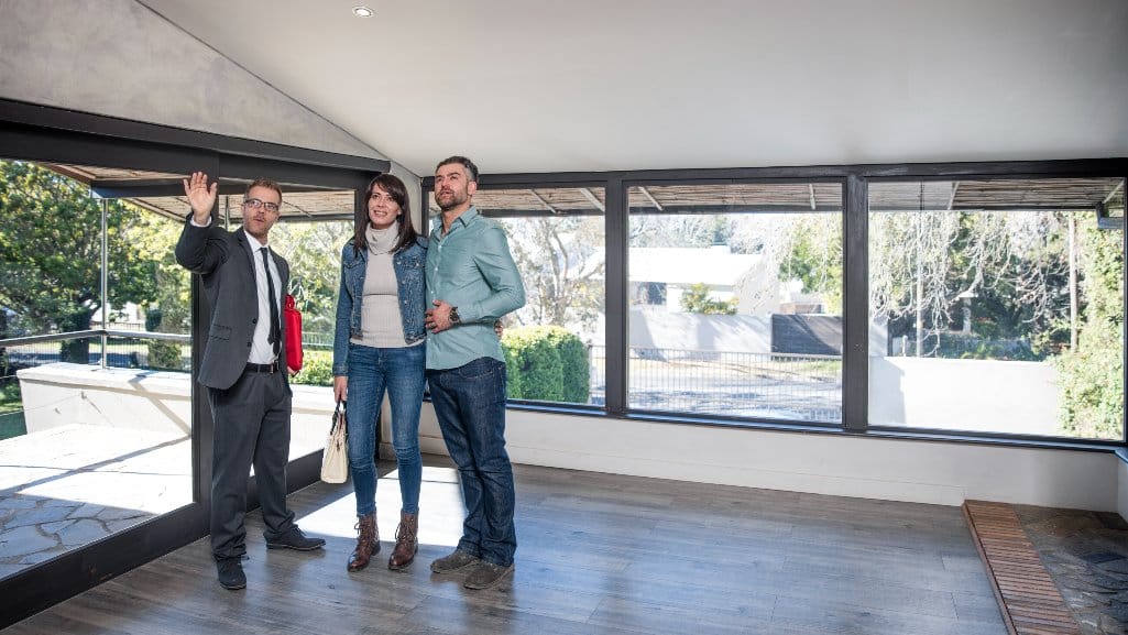 Couple standing in the empty room of a house for sale while their realtor points out details.