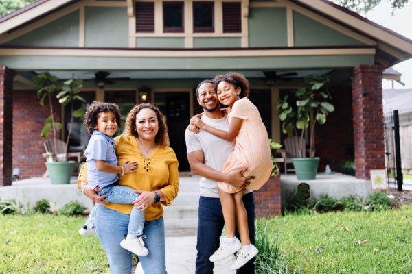 Couple holding their children, while standing in front of their new house purchased with a home mortgage through People Driven Credit Union.