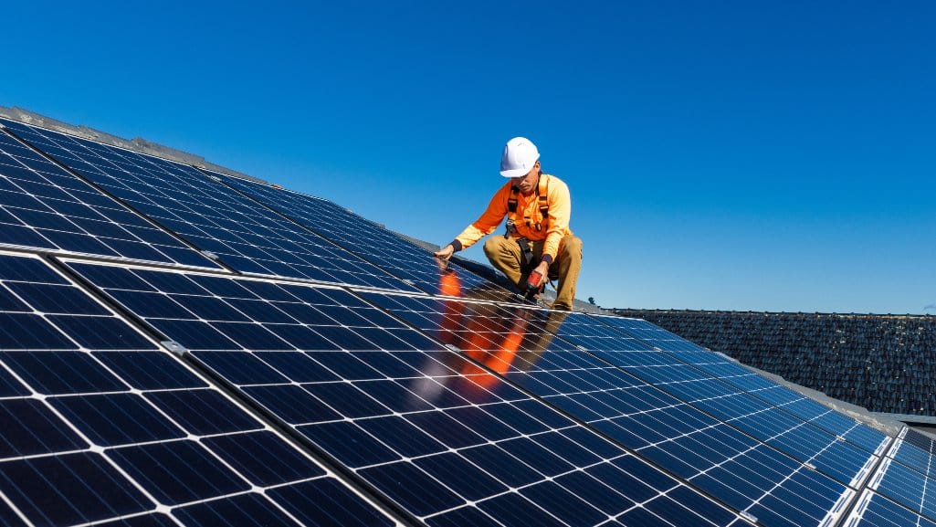 Worker installing solar panels on the roof of a house.