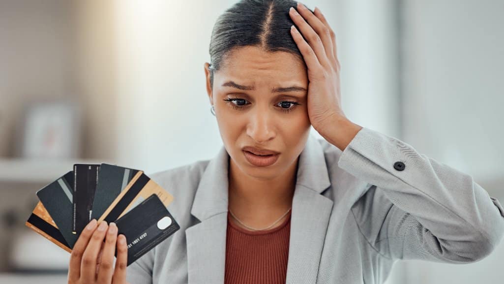 Worried woman holding six credit cards in one hand and her head in the other, wondering if debt consolidation can help her.