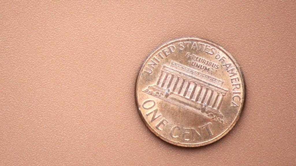 Close-up of a single U.S. one-cent coin on a smooth tan background.