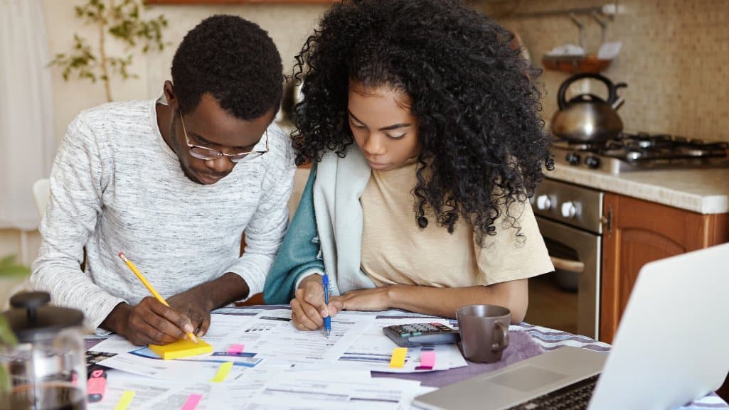 Two people reviewing bills and budgeting at a kitchen table with a laptop and calculator for People Driven Credit Union’s year-end financial checklist.