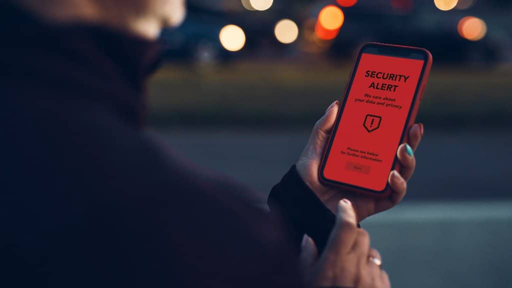 Person holding a smartphone displaying a red “SECURITY ALERT” message on the screen.