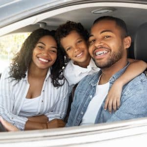Couple with TruStage&reg; Auto Insurance through their People Driven Credit Union membership, posing with their small child while stopped in their car.