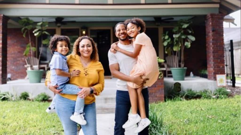 Family of four in Michigan smiling in front of their home after overcoming a financial challenge by building housing plan with People Driven Credit Union.